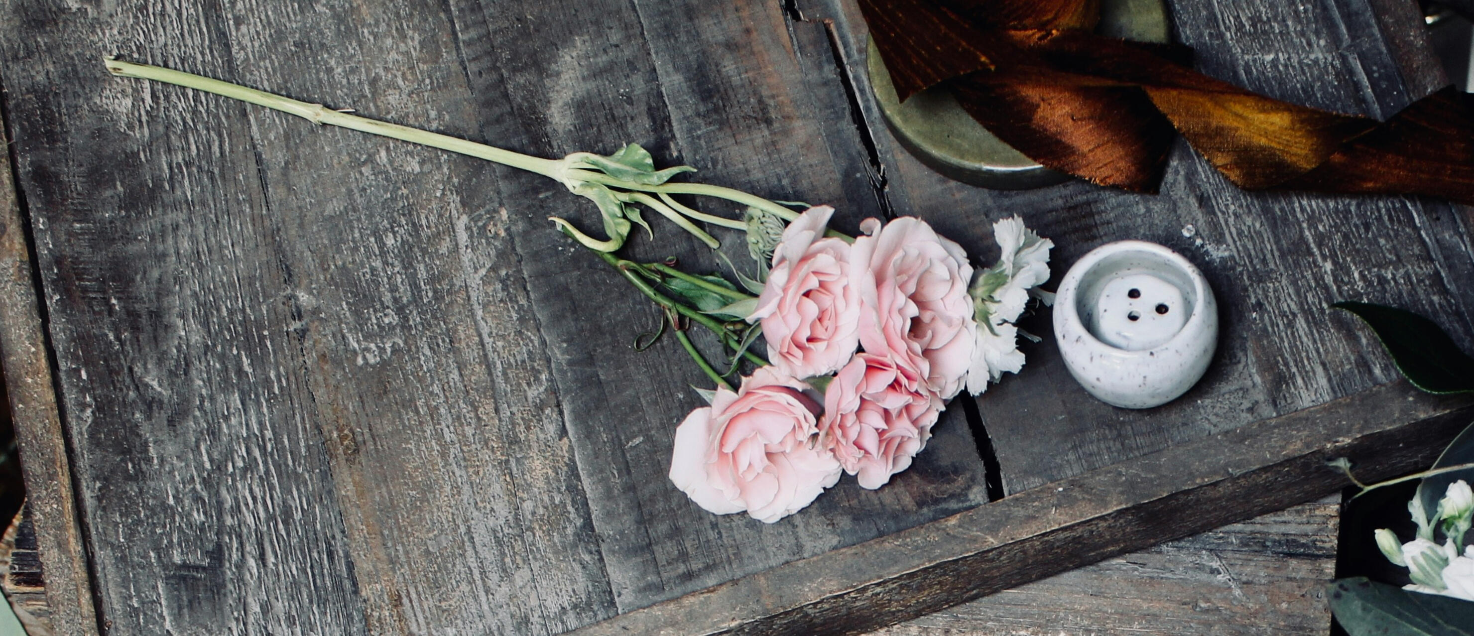 A medium grey table with pale pink flowers on it and a white mixing bowl.